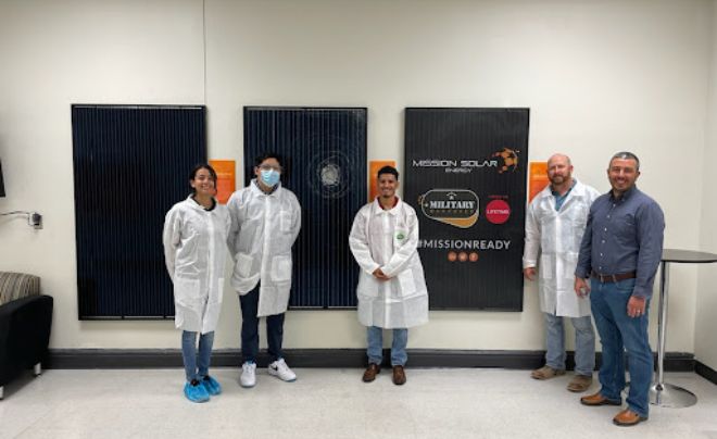 Four people in white lab coats and one person in a button down shirt and jeans