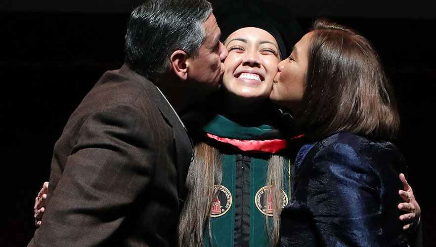 UIWSOM graduate being hooded and receiving kisses from proud parents