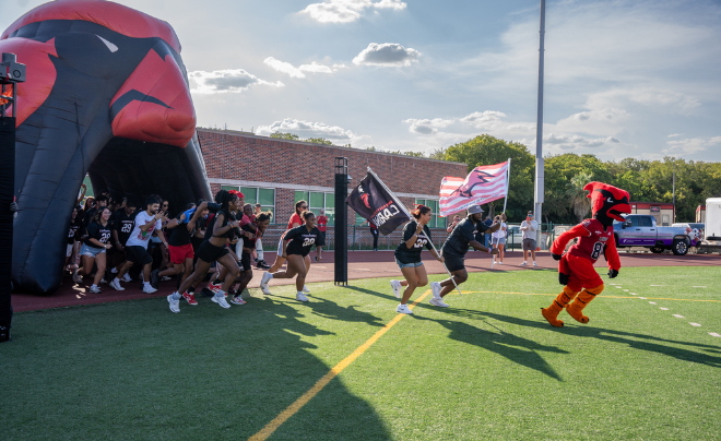 Red the Cardinal and students running across football field